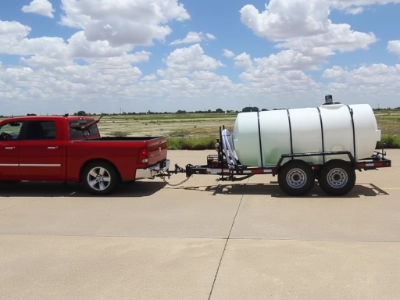 A red truck towing a 1025 water trailer on the road